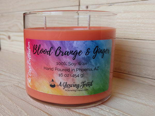 A 16 oz glass tumbler containing an orange Blood Orange and Ginger scented soy candle by A Glowing Trend