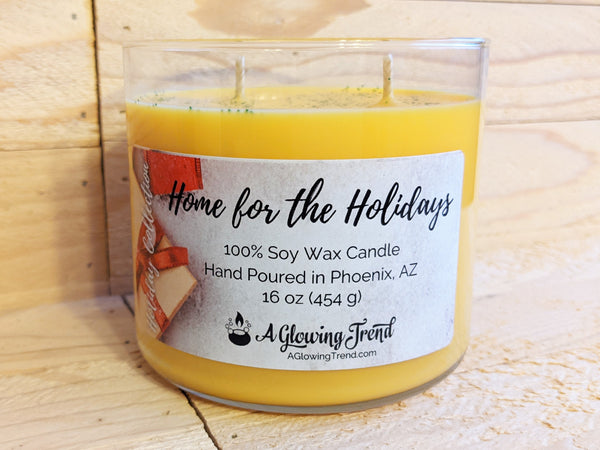 A 16 oz glass tumbler containing a yellow Home for the Holidays scented soy candle topped with glitter by A Glowing Trend.