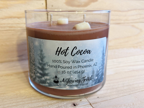 A 16 oz glass tumbler containing a brown Hot Cocoa scented soy candle topped with wax marshmallows by A Glowing Trend.