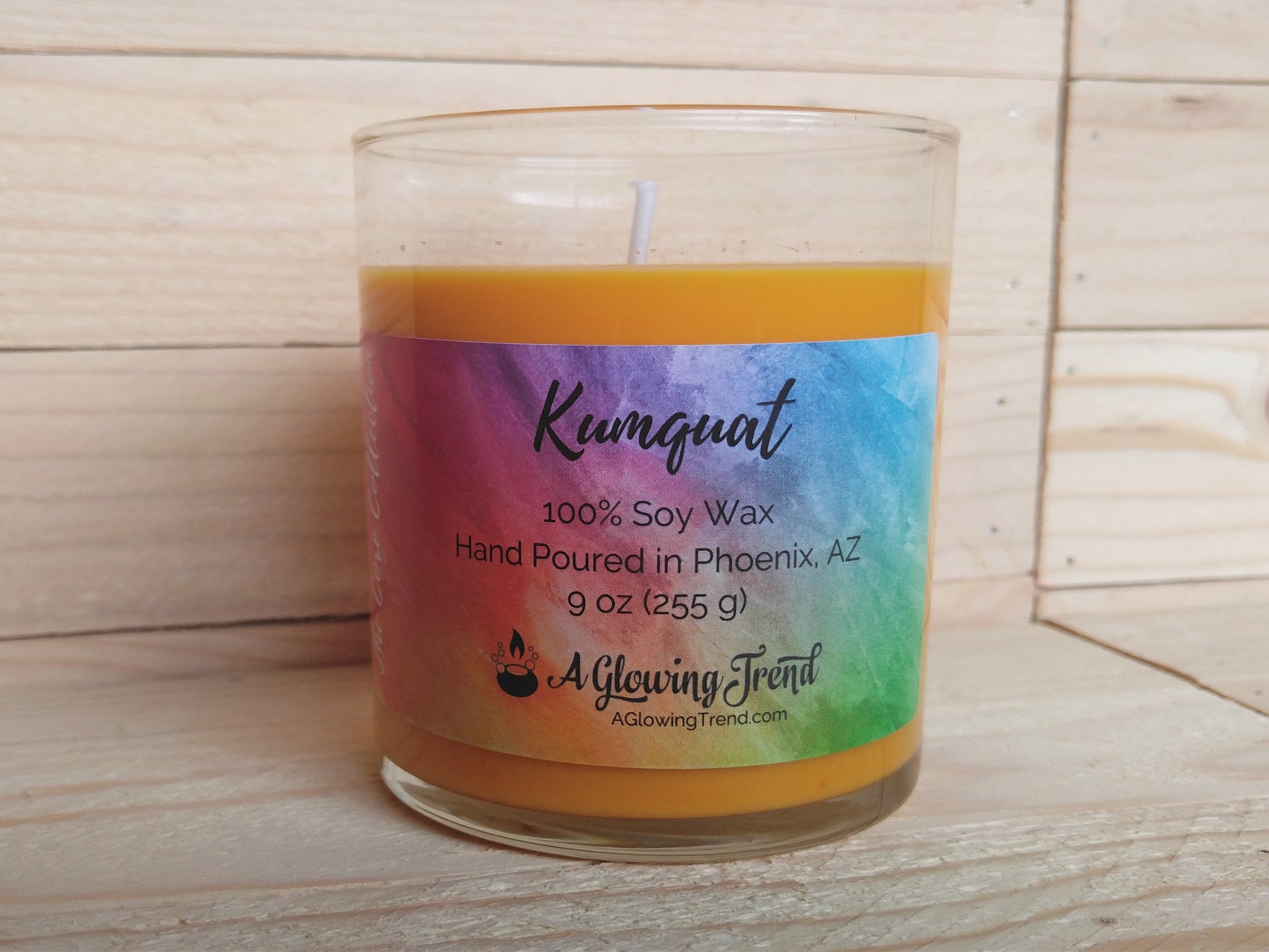 A 9 oz glass tumbler containing a yellow-orange Kumquat scented soy candle by A Glowing Trend