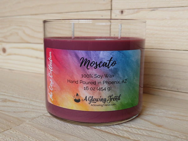A 16 oz glass tumbler containing a reddish-purple Moscato scented soy candle by A Glowing Trend