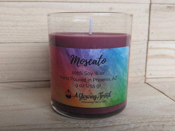A 9 oz glass tumbler containing a reddish-purple Moscato scented soy candle by A Glowing Trend