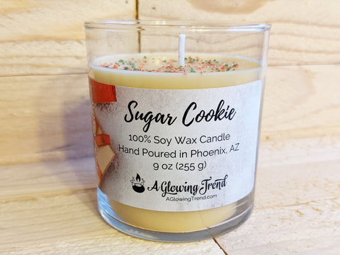 A 9 oz glass tumbler containing a yellow Sugar Cookie scented soy candle topped with red and green sugar sprinkles by A Glowing Trend.