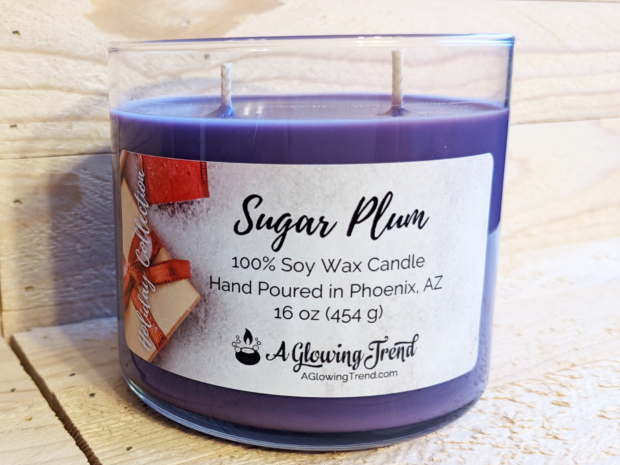 A 16 oz glass tumbler containing a purple Sugar Plum scented soy candle topped with glitter by A Glowing Trend.