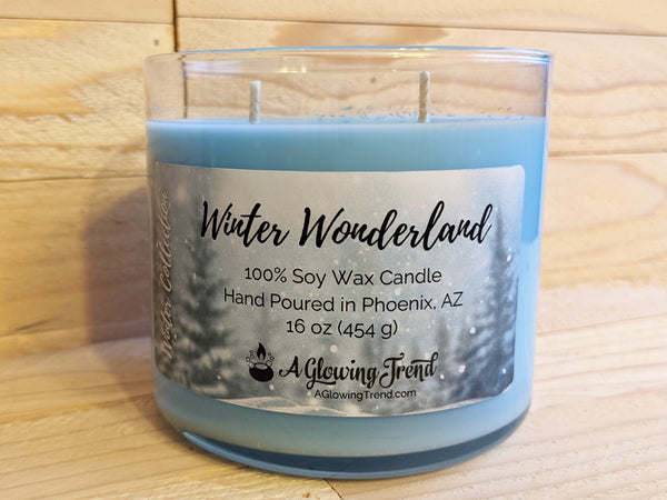 A 16 oz glass tumbler containing a blue Winter Wonderland scented soy candle topped with glitter by A Glowing Trend.