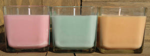 Three square glass containers with pink, green, and oragane Odor Neutralizing candles.