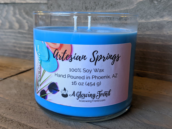 A 16 oz glass tumbler containing a blue Artesian Springs scented soy candle by A Glowing Trend.