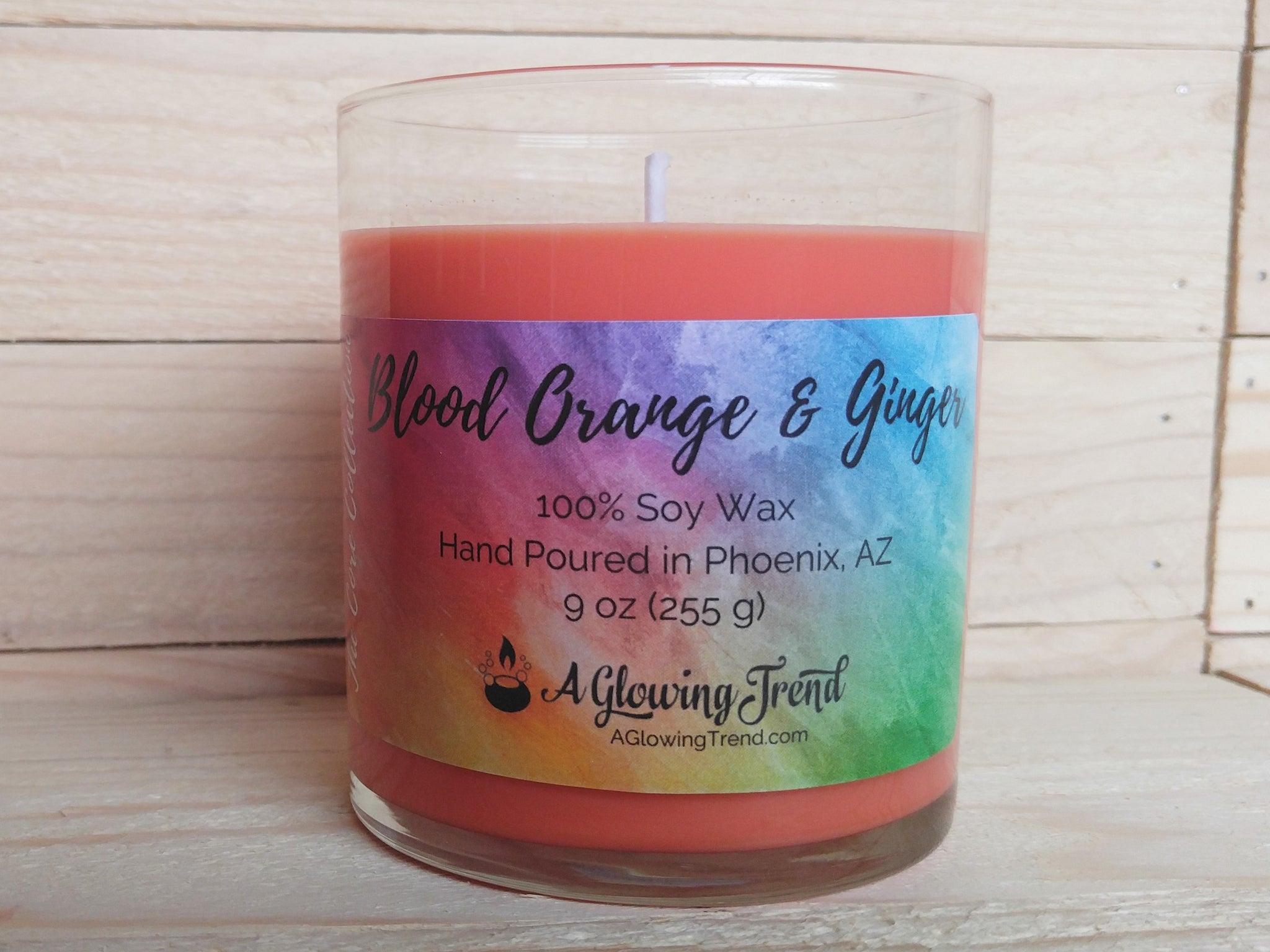 A 9 oz glass tumbler containing an orange Blood Orange and Ginger scented soy candle by A Glowing Trend
