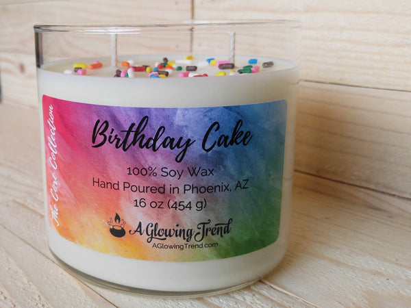 A 16 oz glass tumbler containing a white Birthday Cake scented soy candle topped with sugar sprinkles by A Glowing Trend.