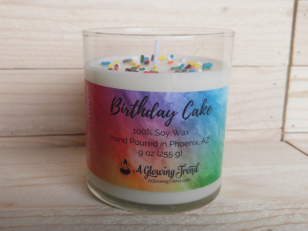 A 9 oz glass tumbler containing a white Birthday Cake scented soy candle topped with sugar sprinkles by A Glowing Trend.