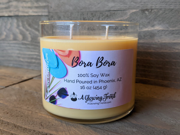 A 16 oz glass tumbler containing a light orange Bora Bora scented soy candle by A Glowing Trend.