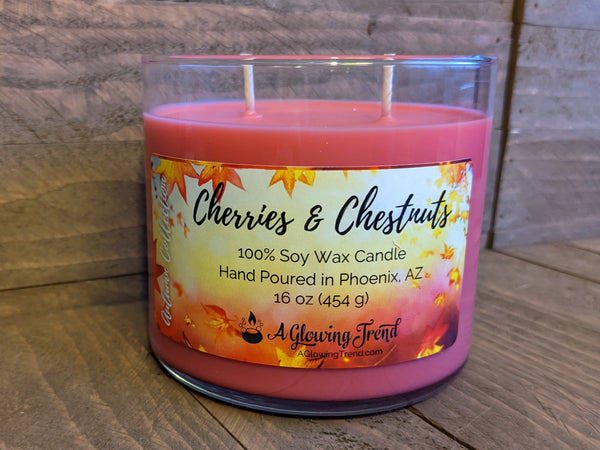 A 16 oz glass tumbler containing a red Cherries and Chestnuts scented soy candle by A Glowing Trend.