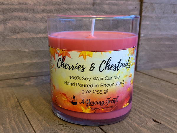 A 9 oz glass tumbler containing a red Cherries and Chestnuts scented soy candle by A Glowing Trend.