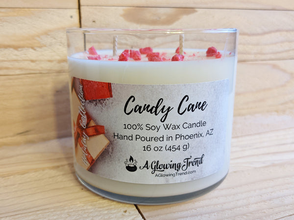 A 16 oz glass tumbler containing a white Candy Cane scented soy candle topped with bits of red wax by A Glowing Trend.