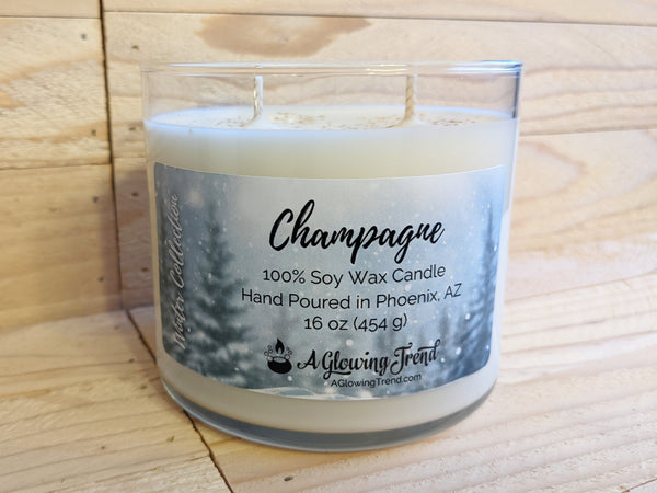 A 16 oz glass tumbler containing a white Champagne scented soy candle topped with glitter by A Glowing Trend.