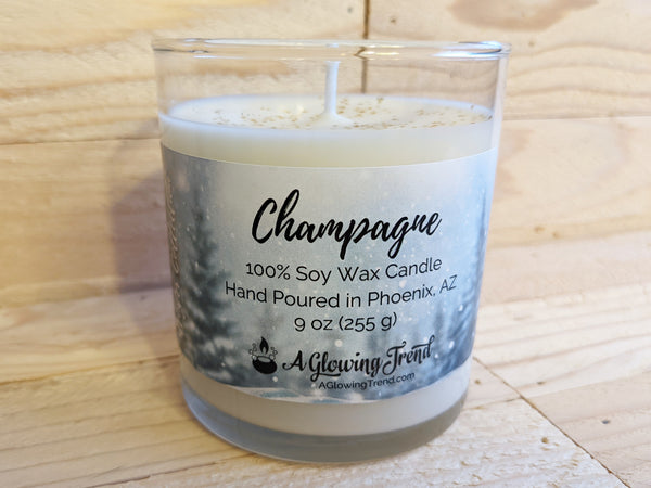 A 9 oz glass tumbler containing a white Champagne scented soy candle topped with glitter by A Glowing Trend.