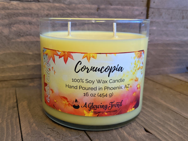 A 16 oz glass tumbler containing a yellow Cornucopia scented soy candle by A Glowing Trend.