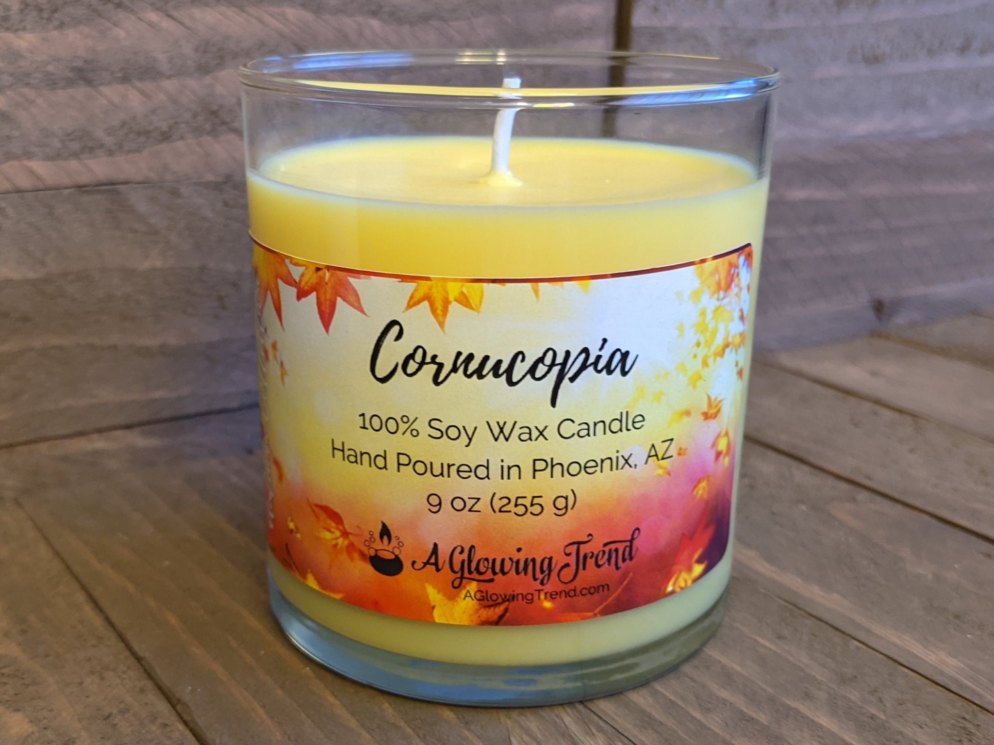 A 9 oz glass tumbler containing a yellow Cornucopia scented soy candle by A Glowing Trend.