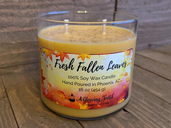 A 16 oz glass tumbler containing a yellow-orange Fresh Fallen Leaves scented soy candle topped with glitter by A Glowing Trend.