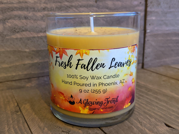 A 9 oz glass tumbler containing a yellow-orange Fresh Fallen Leaves scented soy candle topped with glitter by A Glowing Trend.