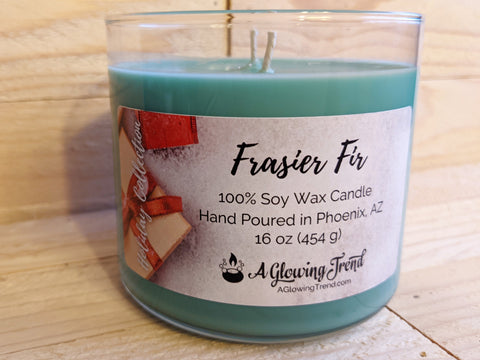 A 16 oz glass tumbler containing a green Frasier Fir scented soy candle by A Glowing Trend.