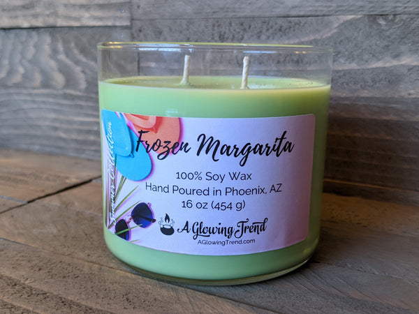 A 16 oz glass tumbler containing a light green Frozen Margarita scented soy candle by A Glowing Trend.