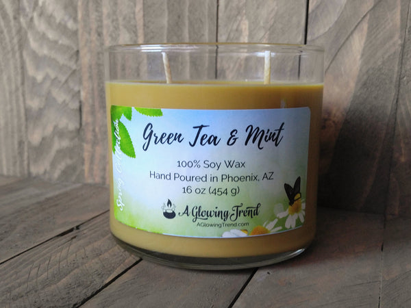 A 16 oz glass tumbler containing a light golden Green Tea and Mint scented soy candle by A Glowing Trend.