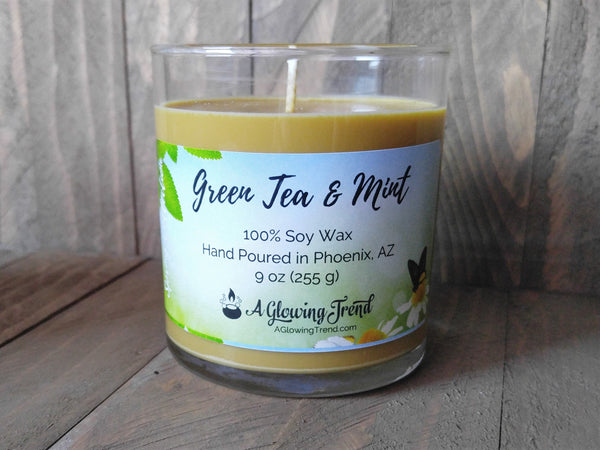 A 9 oz glass tumbler containing a light golden Green Tea and Mint scented soy candle by A Glowing Trend.