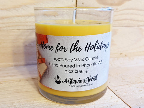 A 9 oz glass tumbler containing a yellow Home for the Holidays scented soy candle topped with glitter by A Glowing Trend.
