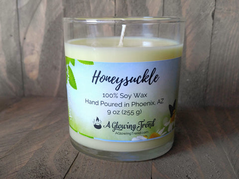 A 9 oz glass tumbler containing a light yellow Honeysuckle scented soy candle by A Glowing Trend.