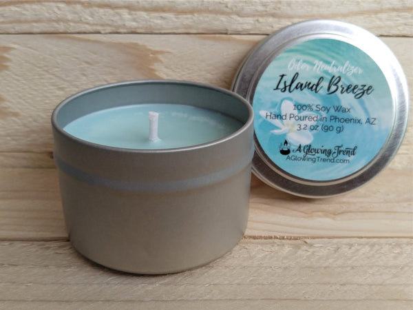 A 3.2 oz round tin containing a light blue Odor Neutralizing Island Breeze scented soy candle by A Glowing Trend.
