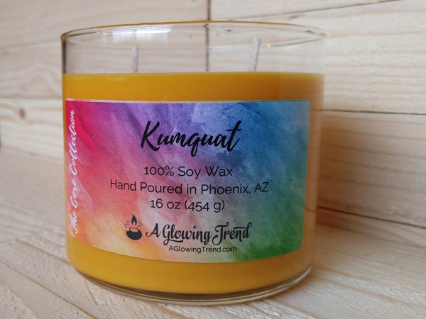 A 16 oz glass tumbler containing a yellow-orange Kumquat scented soy candle by A Glowing Trend