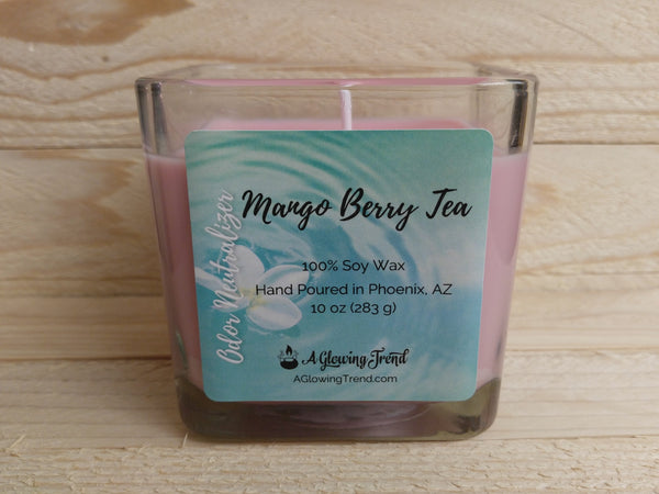 A 10 oz glass square containing a light pink Odor Neutralizing Mango Berry Tea scented soy candle by A Glowing Trend.