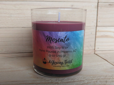 A 9 oz glass tumbler containing a reddish-purple Moscato scented soy candle by A Glowing Trend