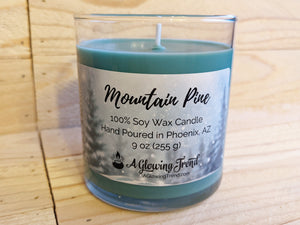 A 9 oz glass tumbler containing a green Mountain Pine scented soy candle by A Glowing Trend