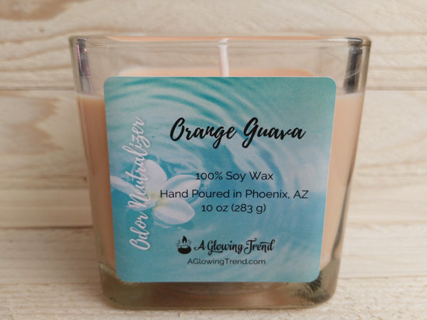 A 10 oz glass square containing a light orange Odor Neutralizing Orange Guava scented soy candle by A Glowing Trend.
