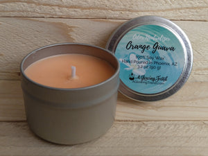 A 3.2 oz round tin containing a light orange Odor Neutralizing Orange Guava scented soy candle by A Glowing Trend.