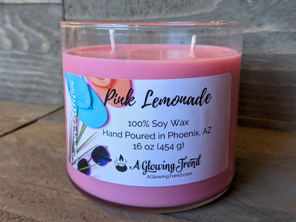 A 16 oz glass tumbler containing a pink Pink Lemonade scented soy candle by A Glowing Trend.
