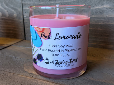 A 9 oz glass tumbler containing a pink Pink Lemonade scented soy candle by A Glowing Trend.