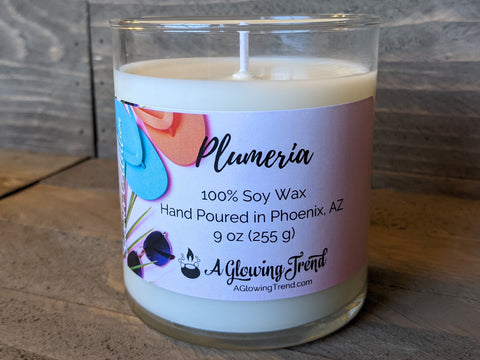 A 9 oz glass tumbler containing a white Plumeria scented soy candle by A Glowing Trend.