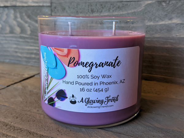 A 16 oz glass tumbler containing a purple Pomegranate scented soy candle by A Glowing Trend.