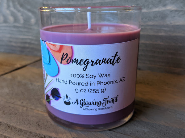 A 9 oz glass tumbler containing a purple Pomegranate scented soy candle by A Glowing Trend.