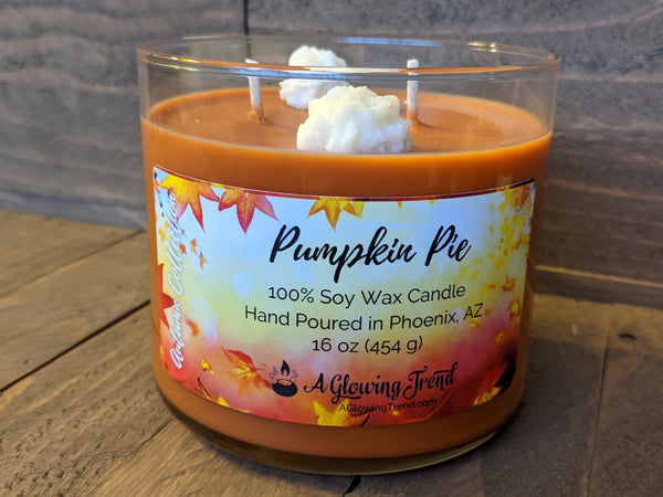 A 16 oz glass tumbler containing an orange Pumpkin Pie scented soy candle topped with two wax whipped cream dollops by A Glowing Trend.