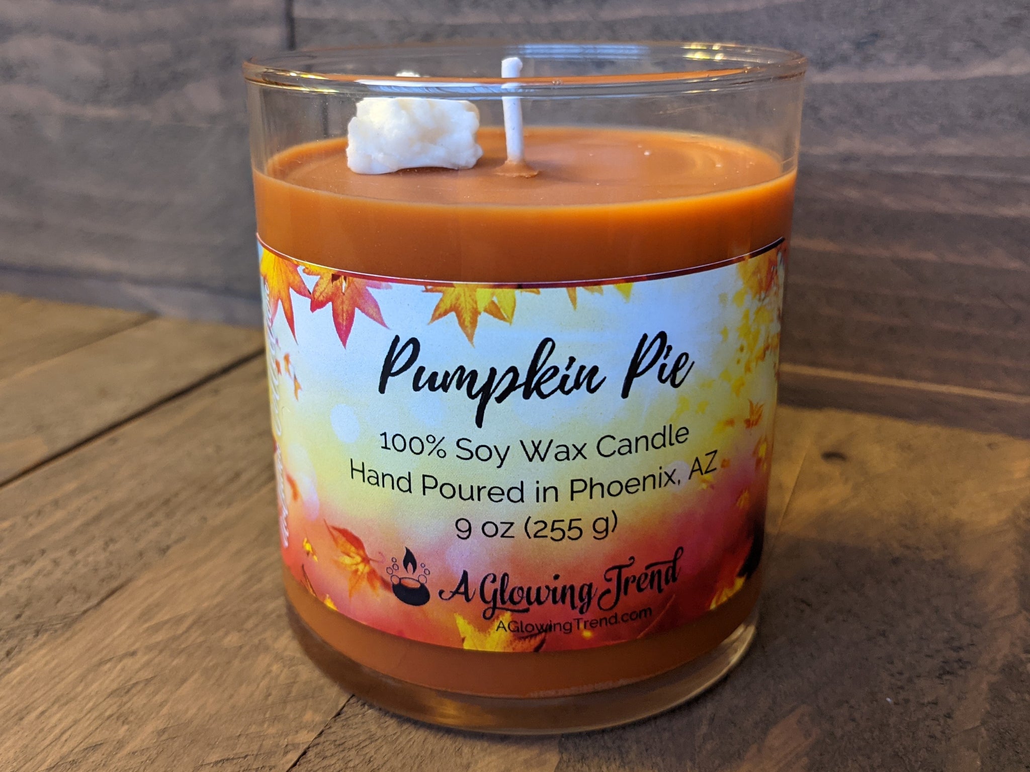 A 9 oz glass tumbler containing an orange Pumpkin Pie scented soy candle topped with a wax whipped cream dollop by A Glowing Trend.