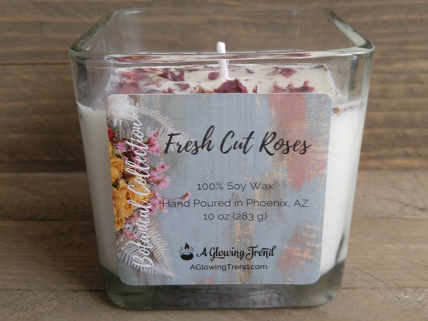 A 10 oz glass square containing a white Fresh Cut Roses scented soy candle topped with dried rose petals by A Glowing Trend.