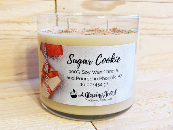 A 16 oz glass tumbler containing a yellow Sugar Cookie scented soy candle topped with red and green sugar sprinkles by A Glowing Trend.