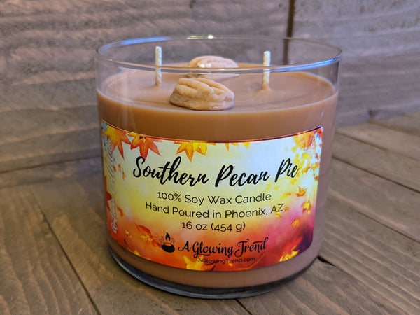 A 16 oz glass tumbler containing a brown Southern Pecan Pie scented soy candle topped with two wax pecans by A Glowing Trend.
