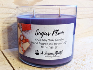 A 16 oz glass tumbler containing a purple Sugar Plum scented soy candle topped with glitter by A Glowing Trend.