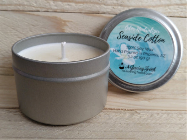 A 3.2 oz round tin containing a white Odor Neutralizing Seaside Cotton scented soy candle by A Glowing Trend.