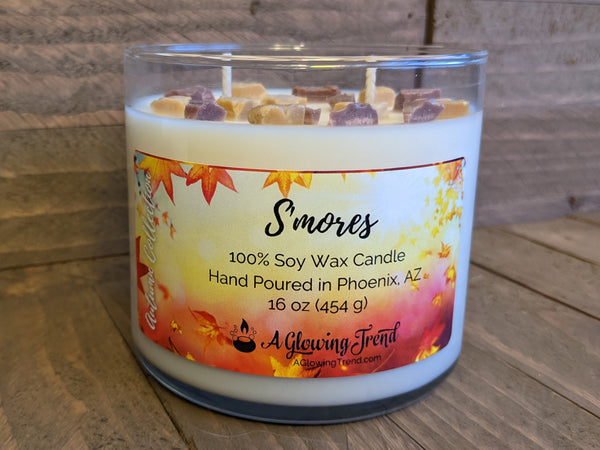 A 16 oz glass tumbler containing a white S'mores scented soy candle topped with wax graham cracker and chocolate bits by A Glowing Trend.
